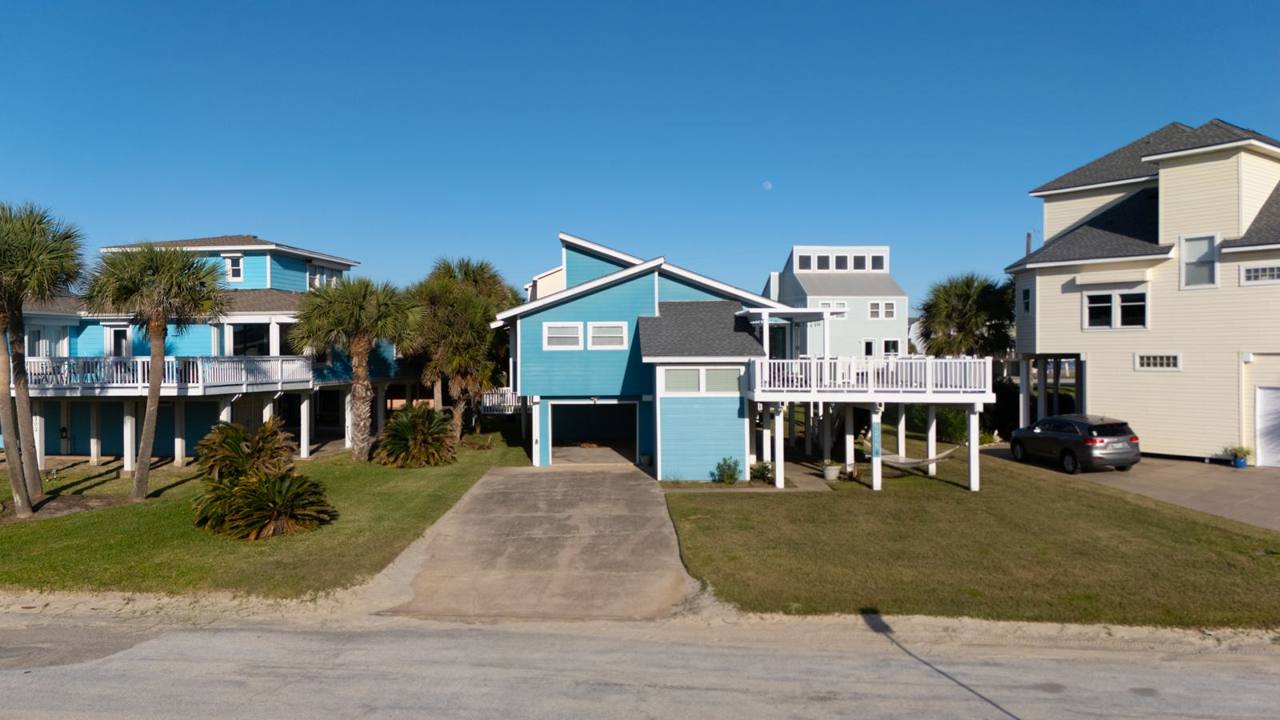 Front of the house: a turquoise raised beach house with a large deck and a driveway