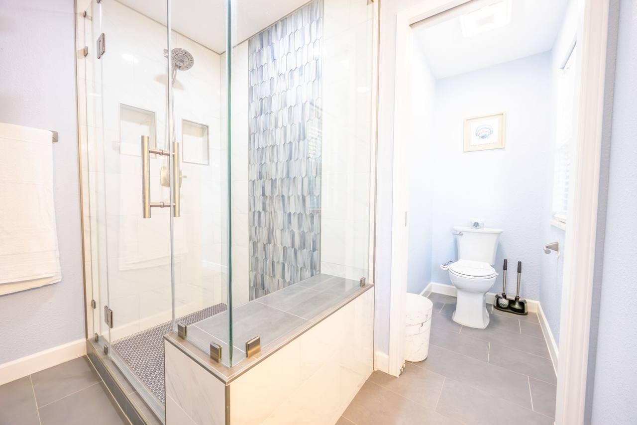 Same bathroom: glass walk-in shower with a built-in bench and a separate toilet room